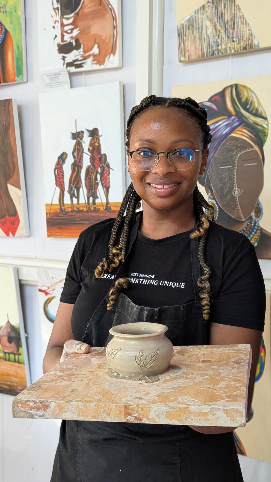 Joan Githinji smiling, holding a finished clay pot in a pottery studio